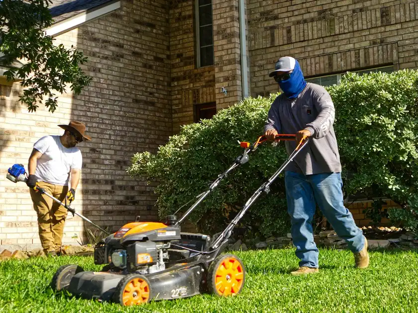 Two landscapers mowing and trimming a front lawn